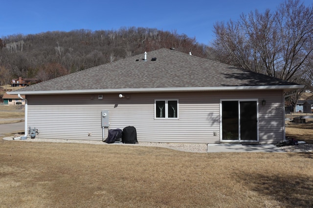 rear view of house featuring a yard and roof with shingles