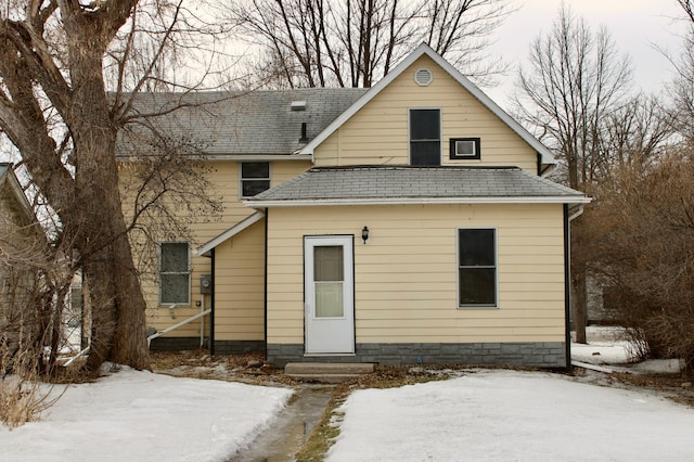 snow covered house with entry steps and a shingled roof