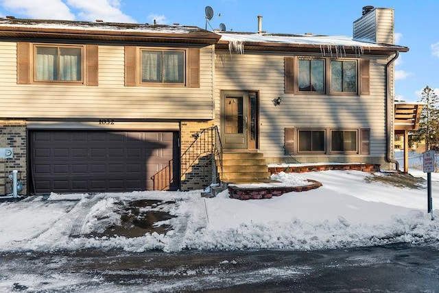 split foyer home with a garage, brick siding, and a chimney