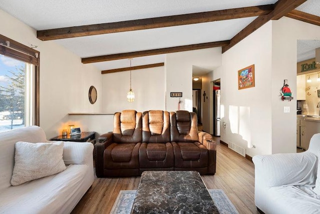 living room featuring vaulted ceiling with beams, light wood-style floors, and visible vents