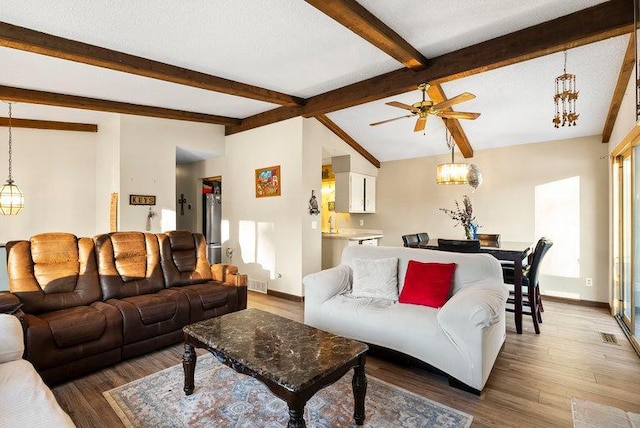 living area with lofted ceiling with beams, a textured ceiling, baseboards, and wood finished floors