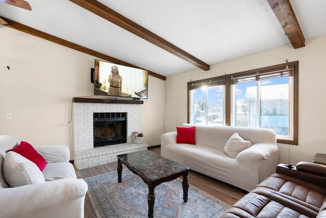 living room with a brick fireplace, lofted ceiling with beams, a textured ceiling, and wood finished floors