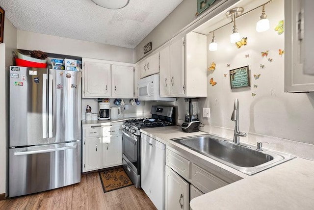 kitchen with white cabinets, stainless steel appliances, a textured ceiling, light wood-style floors, and a sink