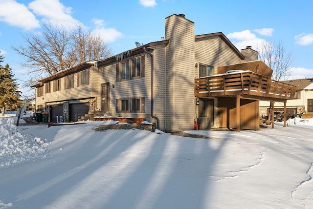 snow covered rear of property featuring a deck, a chimney, and an attached garage