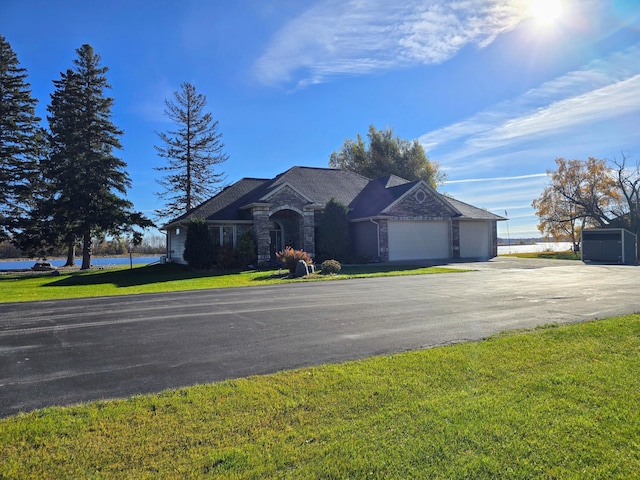 view of front of home with driveway, a garage, stone siding, a water view, and a front yard