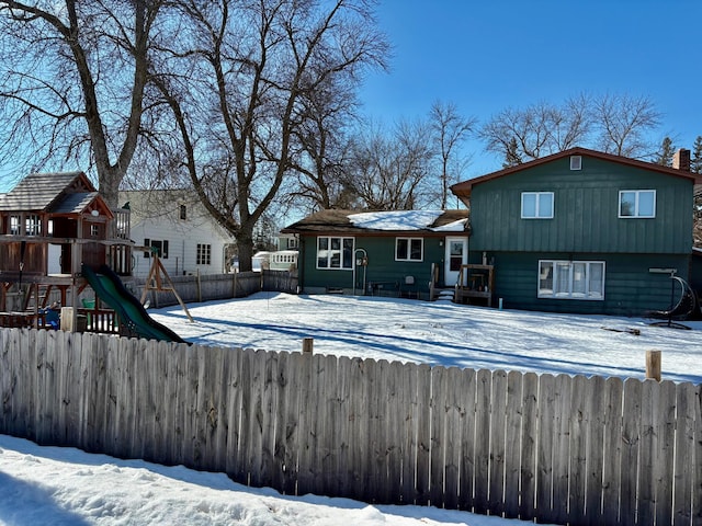 snow covered rear of property with a playground and fence private yard