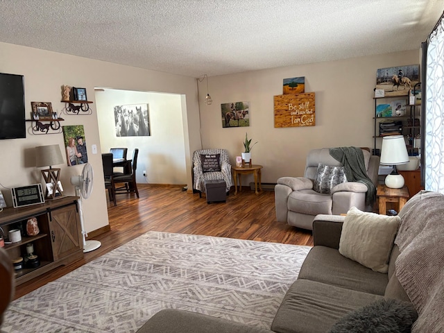 living area featuring a baseboard heating unit, a textured ceiling, baseboards, and wood finished floors