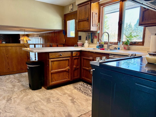 kitchen featuring a peninsula, a sink, light countertops, and brown cabinets