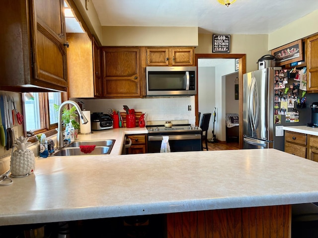 kitchen with a peninsula, a sink, light countertops, appliances with stainless steel finishes, and brown cabinetry