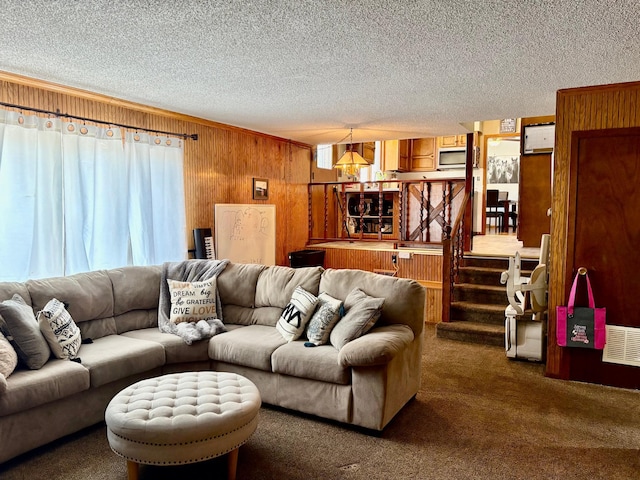 carpeted living room featuring wooden walls, visible vents, stairway, and a textured ceiling