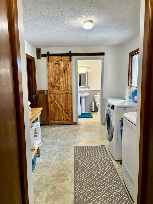 laundry room with a barn door, a sink, a textured ceiling, separate washer and dryer, and laundry area