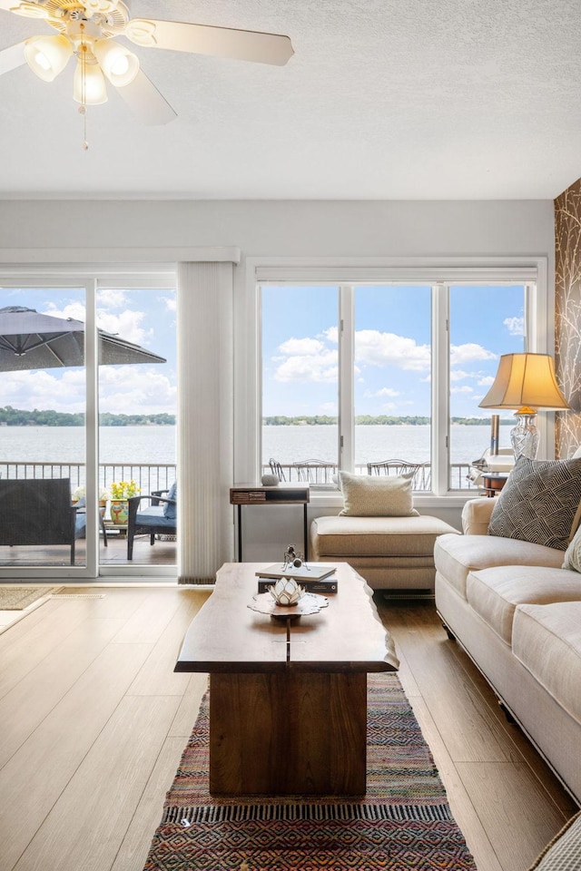 living area with a textured ceiling, ceiling fan, a water view, and wood finished floors