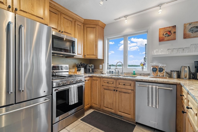 kitchen with light tile patterned floors, brown cabinets, light stone countertops, stainless steel appliances, and a sink