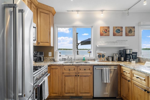 kitchen with light stone countertops, stainless steel appliances, a sink, visible vents, and brown cabinets