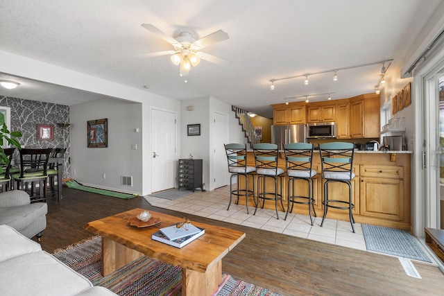 living room featuring wallpapered walls, visible vents, light wood-style flooring, an accent wall, and stairs