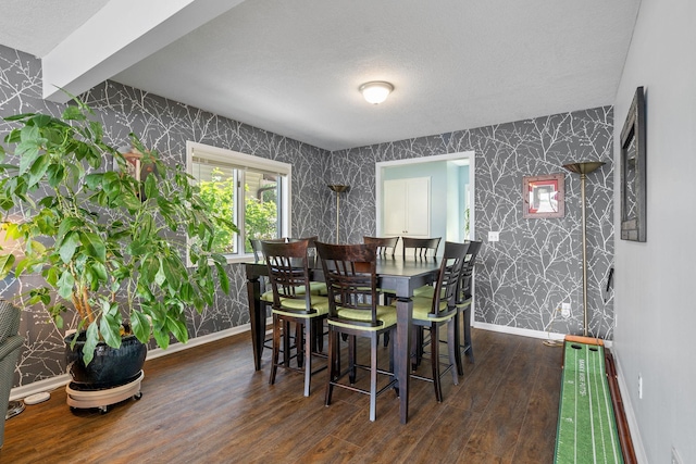 dining room with baseboards, a textured ceiling, wood finished floors, and wallpapered walls