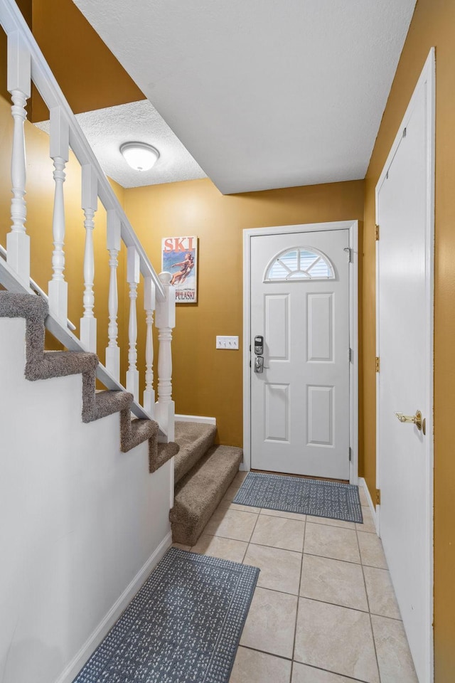 foyer featuring stairs, a textured ceiling, baseboards, and light tile patterned floors