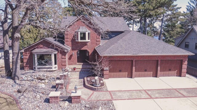 view of front of house with an attached garage, roof with shingles, driveway, and brick siding