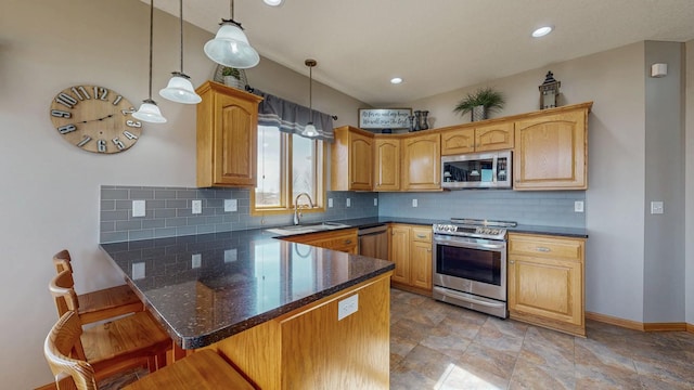 kitchen with a peninsula, a sink, hanging light fixtures, appliances with stainless steel finishes, and a kitchen breakfast bar