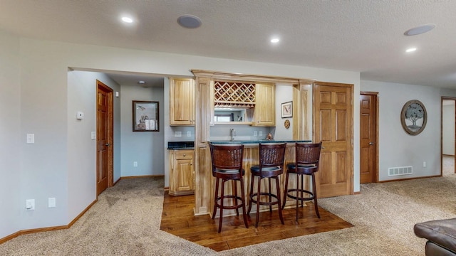 kitchen with visible vents, a kitchen bar, dark countertops, and carpet flooring