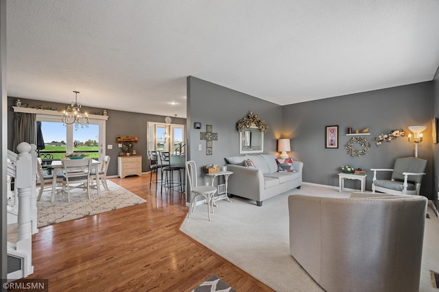 living area featuring baseboards, a textured ceiling, a chandelier, and wood finished floors