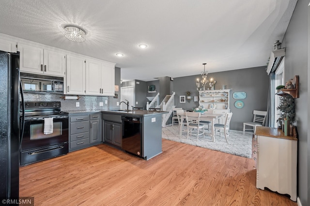 kitchen with a notable chandelier, white cabinets, a peninsula, dark countertops, and black appliances