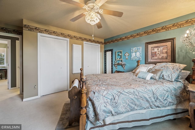 bedroom with carpet flooring, a textured ceiling, two closets, baseboards, and ceiling fan