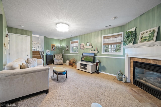 carpeted living room featuring a textured ceiling, visible vents, baseboards, a tiled fireplace, and stairway