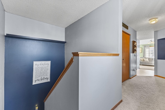 hall with an upstairs landing, carpet flooring, a textured ceiling, and baseboards