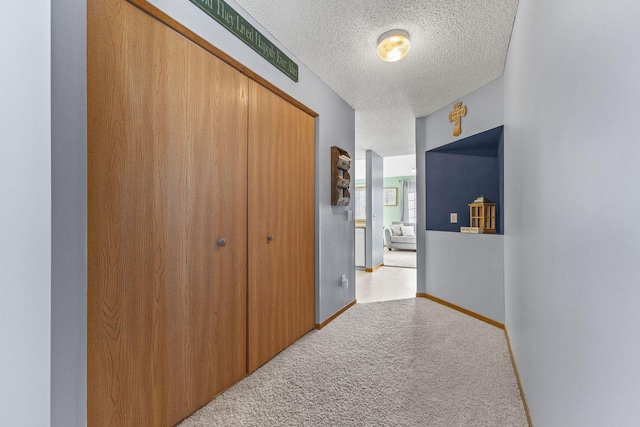 hallway with light colored carpet, a textured ceiling, and baseboards