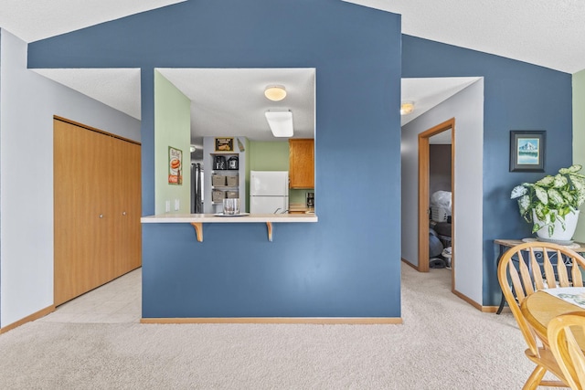 kitchen featuring freestanding refrigerator, vaulted ceiling, light countertops, a kitchen breakfast bar, and light colored carpet