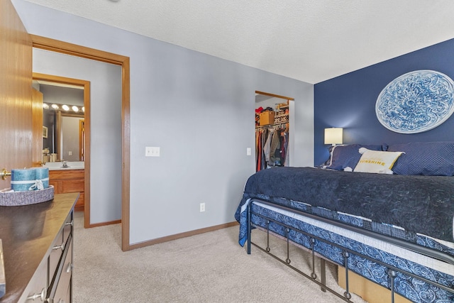 bedroom featuring a sink, a textured ceiling, baseboards, light colored carpet, and a spacious closet