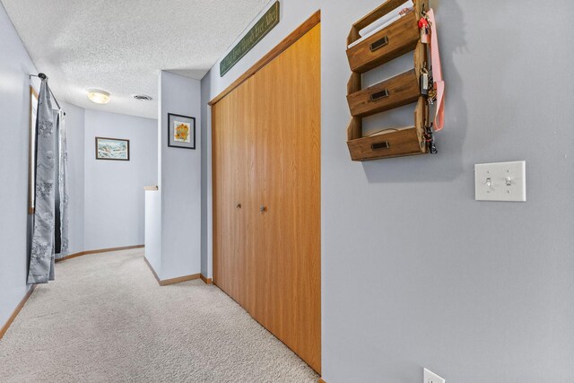 hallway with a textured ceiling, baseboards, and light carpet