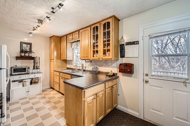 kitchen featuring a healthy amount of sunlight, light floors, a sink, glass insert cabinets, and dark countertops