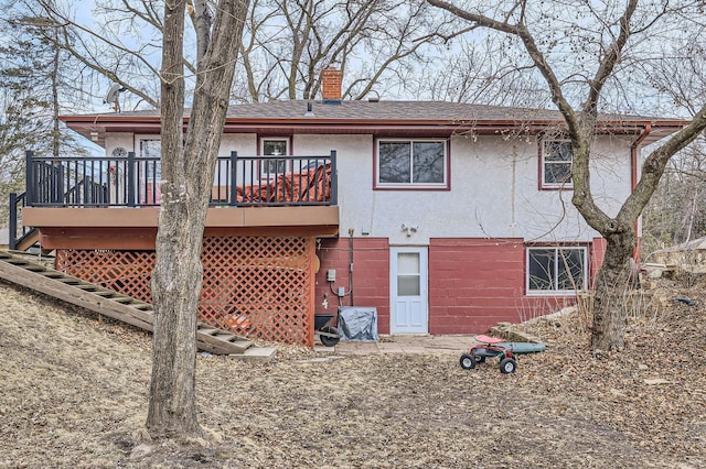 rear view of house with stucco siding, roof with shingles, a wooden deck, and a chimney