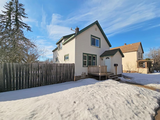 snow covered house featuring a chimney, fence, and a deck