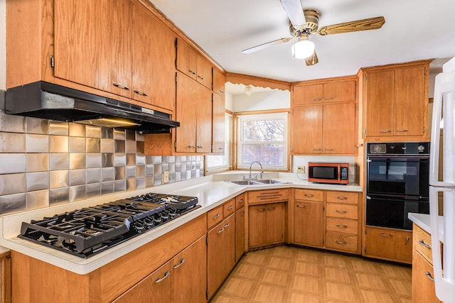 kitchen featuring under cabinet range hood, light floors, light countertops, black appliances, and a sink