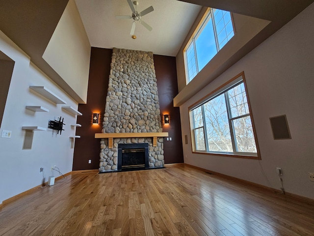 unfurnished living room featuring a stone fireplace, a high ceiling, wood finished floors, and ceiling fan