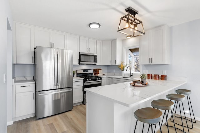 kitchen featuring light wood finished floors, appliances with stainless steel finishes, a peninsula, a kitchen bar, and a sink