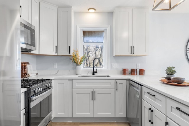 kitchen featuring stainless steel appliances, white cabinetry, a sink, and light stone countertops