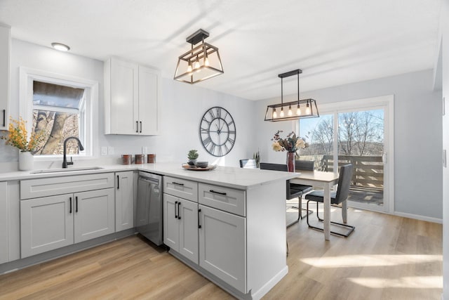 kitchen featuring a peninsula, a sink, hanging light fixtures, stainless steel dishwasher, and light wood finished floors