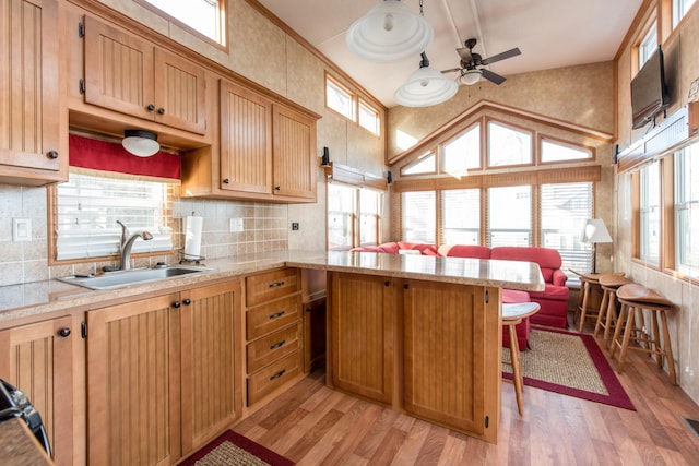 kitchen featuring a peninsula, light wood-type flooring, a ceiling fan, and a sink