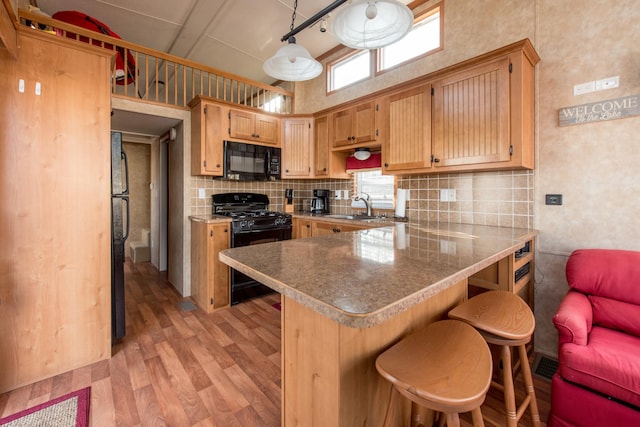 kitchen featuring backsplash, light wood-style flooring, a peninsula, black appliances, and a sink