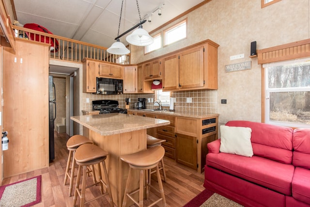 kitchen with light wood-type flooring, black appliances, backsplash, light countertops, and a towering ceiling