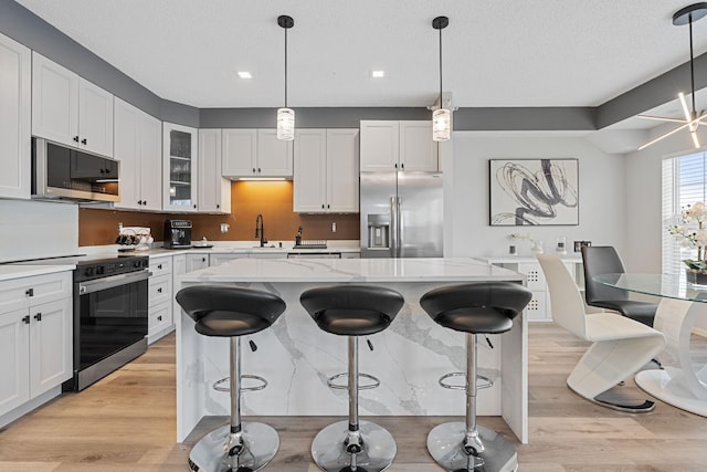 kitchen featuring a center island, light wood-style flooring, appliances with stainless steel finishes, white cabinetry, and a sink