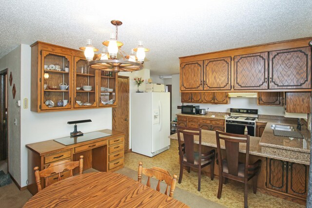 kitchen featuring under cabinet range hood, a sink, white appliances, brown cabinetry, and a chandelier