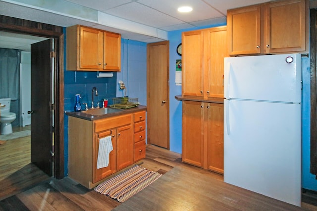 kitchen featuring a sink, backsplash, dark countertops, freestanding refrigerator, and light wood-style floors