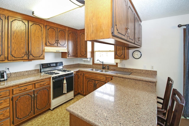 kitchen with a textured ceiling, white gas range oven, brown cabinets, and under cabinet range hood