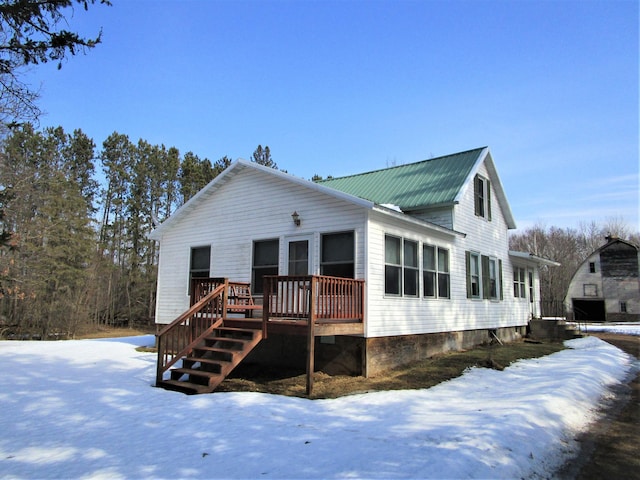 snow covered rear of property featuring stairway, metal roof, and a deck