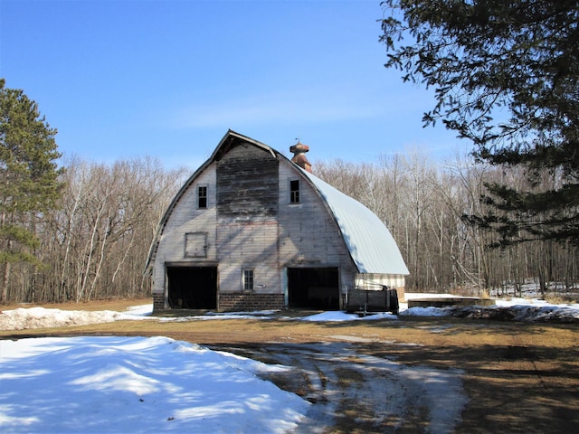 view of snowy exterior with a barn, a garage, a gambrel roof, an outbuilding, and brick siding